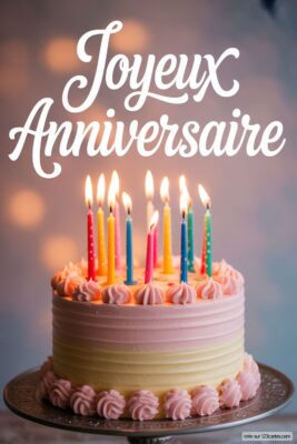 Gâteau d'anniversaire bicolore rose et jaune, avec bougies multicolores allumées, sur fond flou bleu-gris.