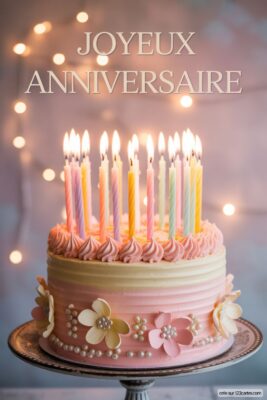 Gâteau d'anniversaire rose et crème, décoré de fleurs et perles, avec 15 bougies allumées.