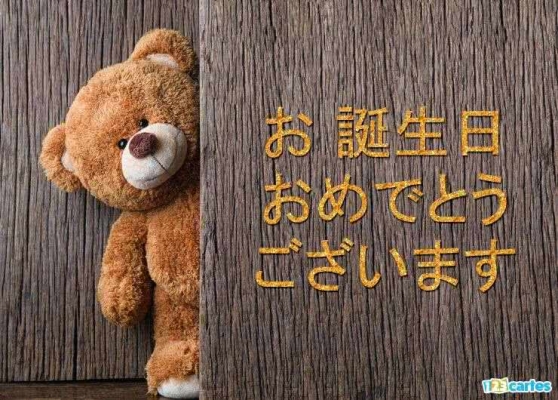 Ours en peluche brun souriant derrière une planche de bois, avec des caractères japonais inscrits en jaune à droite.