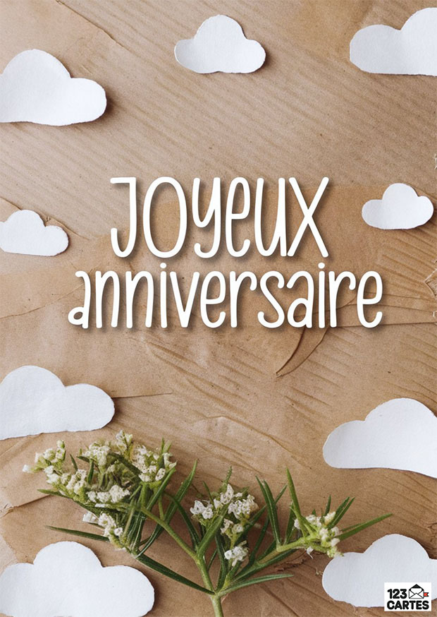 Joyeux anniversaire écrit en blanc sur fond de papier kraft avec fleurs blanches et nuages découpés en papier.